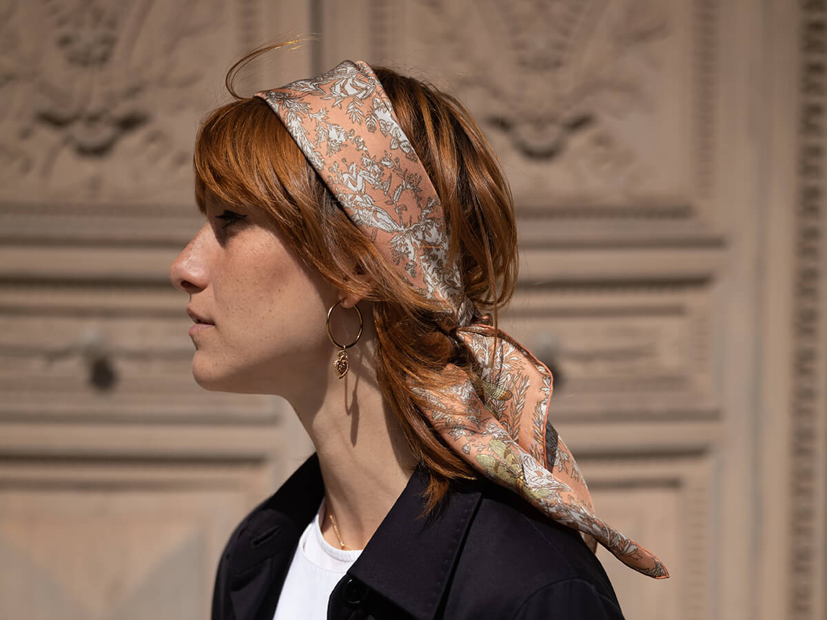 femme aux cheveux chatains portant un foulard en soie rose avec motif végétal et libellule et une veste noire