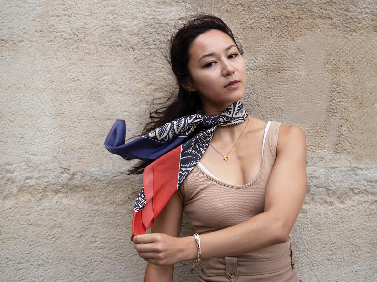 jeune femme aux cheveux noirs portant un débardeur beige et un foulard en soie coton et soie rouge et navy autour du cou